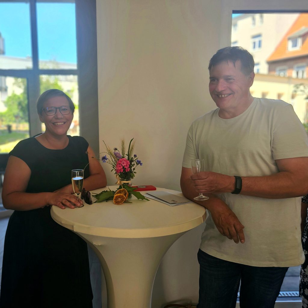 Zwei Personen stehen an einem Stehtisch mit Blumenarrangement