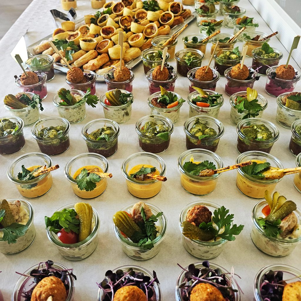 Kleine Gl&auml;ser mit verschiedenen Vorspeisen und Canap&eacute;s auf einem Tisch arrangiert.