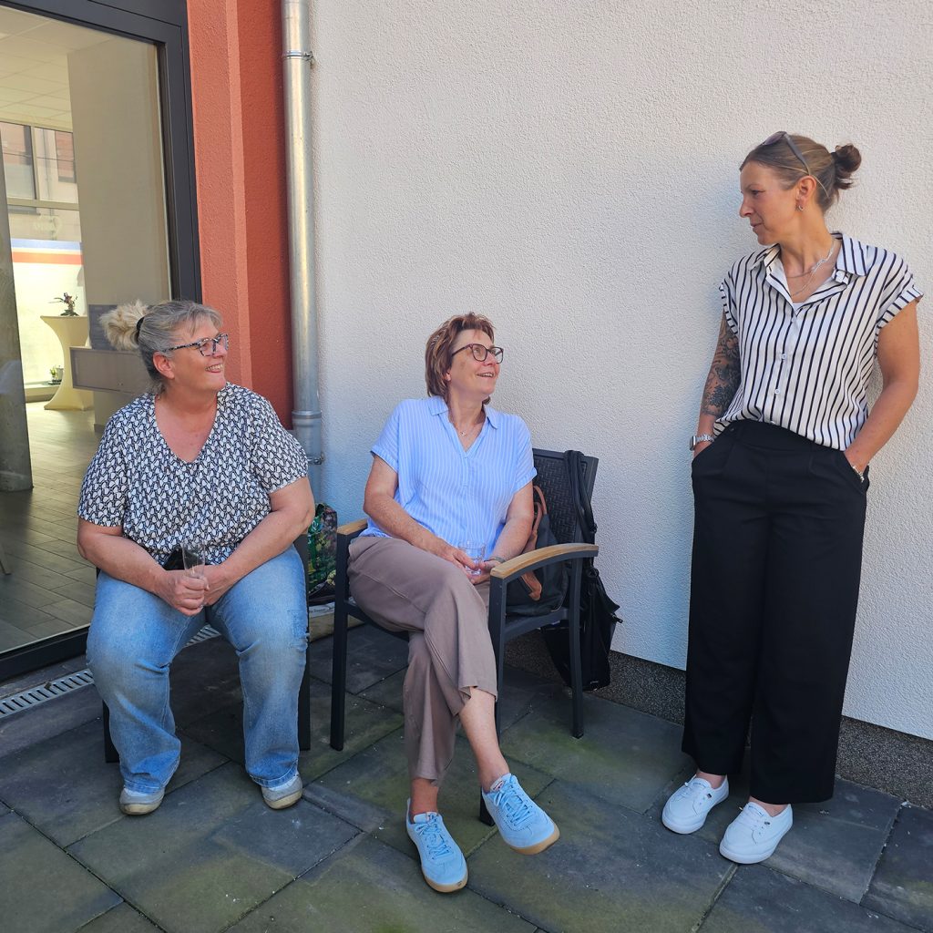 Drei Frauen im Gespr&auml;ch vor einer wei&szlig;en Wand.
