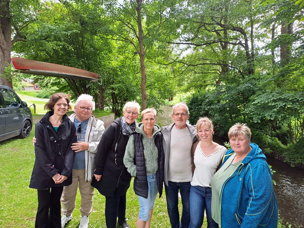 Gruppe von sieben Personen im Freien, umgeben von Bäumen neben einem Fluss oder Bach.