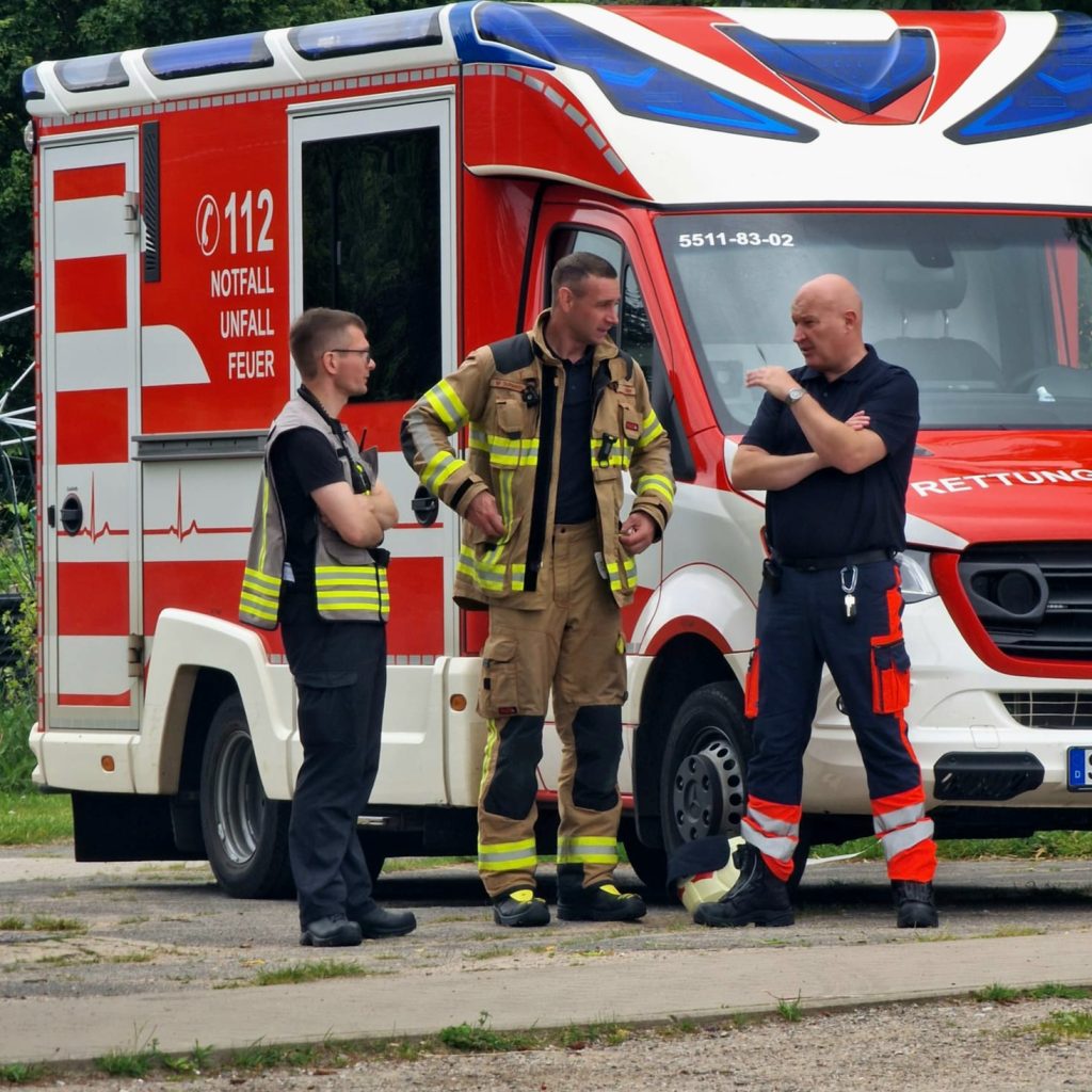 Drei Einsatzkr&auml;fte vor einem Rettungsfahrzeug
