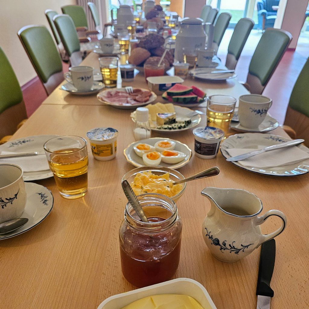 Ein gedeckter Tisch mit Fr&uuml;hst&uuml;cksutensilien in einem Raum mit gr&uuml;n gepolsterten St&uuml;hlen