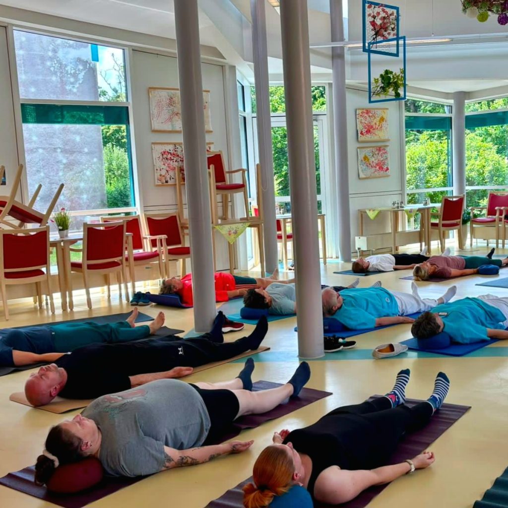 Eine Gruppe von Menschen liegt entspannt auf Yogamatten in einem hellen Raum.