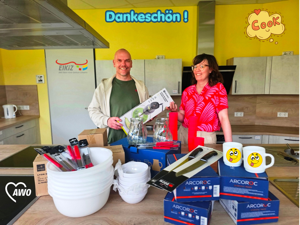 Ein Mann und eine Frau stehen in einer Küche mit gelben Wänden, umgeben von verschiedenen neuen Küchenutensilien, und lächeln.