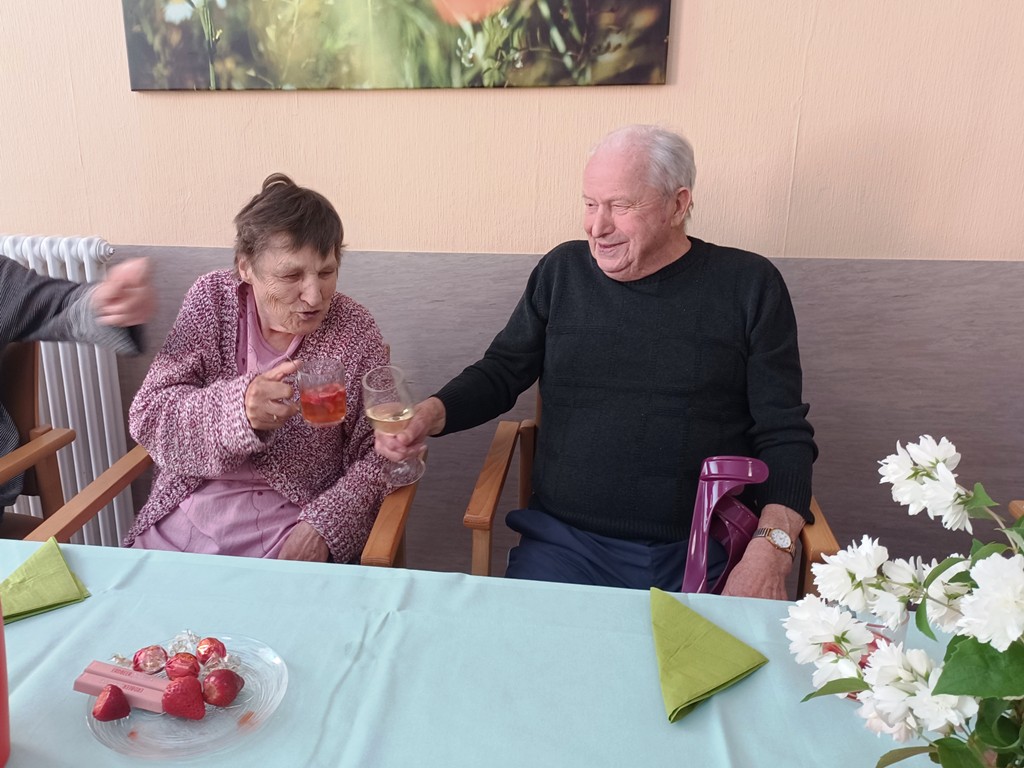 Zwei ältere Menschen stoßen mit Getränken an.