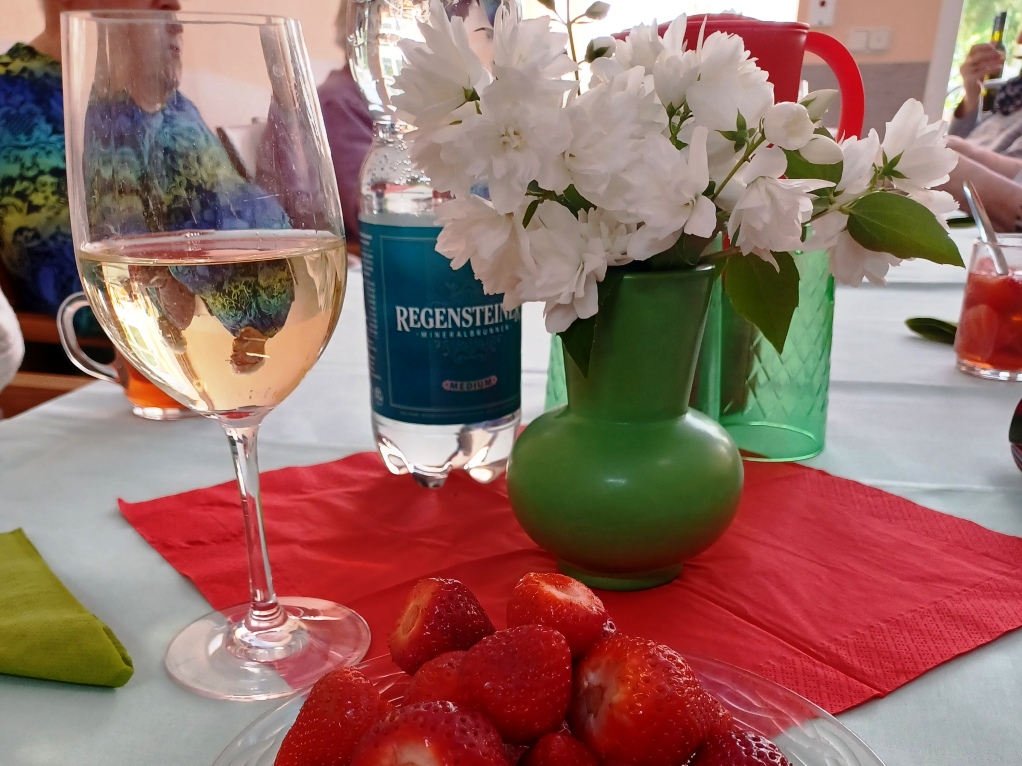 Ein gedeckter Tisch mit einem Weinglas, einem Blumenstrauß in einer Vase und Erdbeeren.