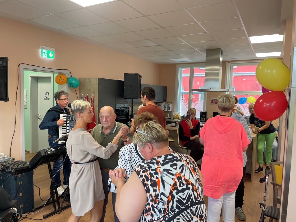 Menschen feiern bei einem Fest in einem Gemeinschaftsraum mit Luftballons und Musik.