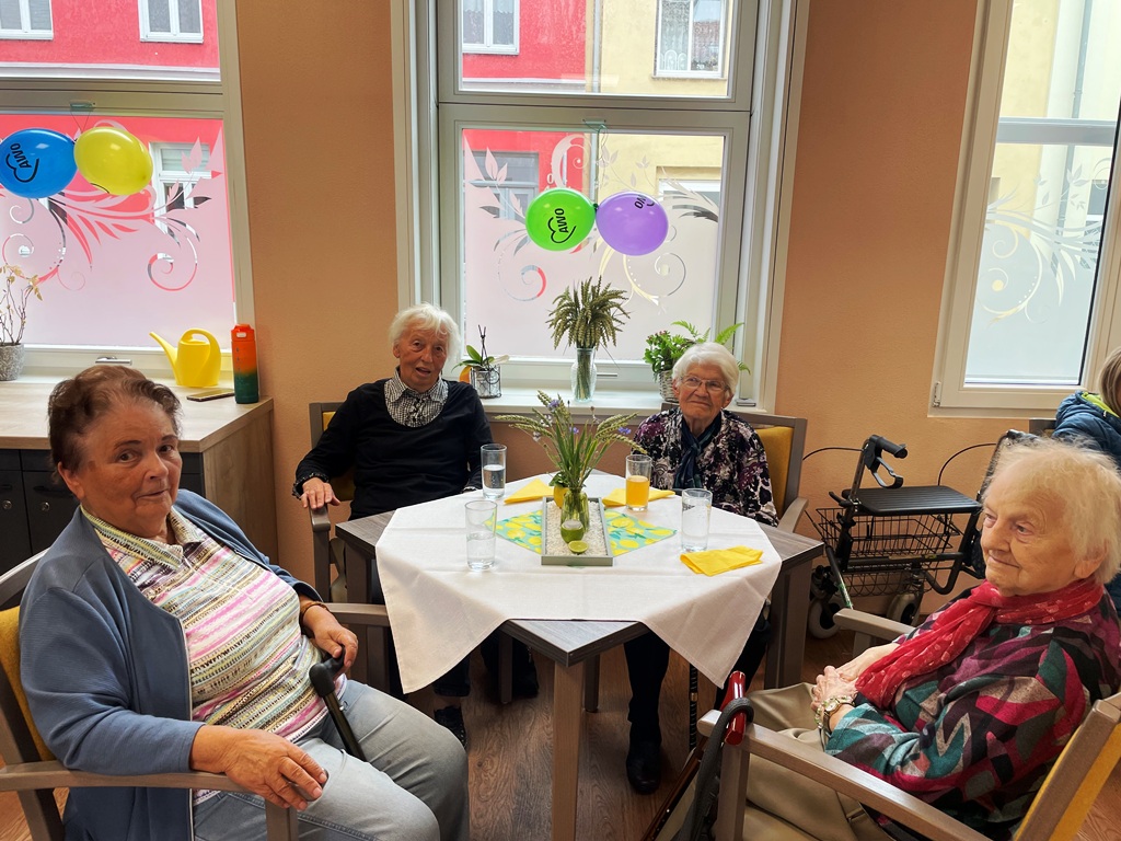 Vier ältere Frauen sitzen an einem Tisch in einem Gemeinschaftsraum.