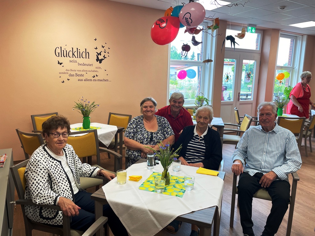 Gruppenfoto von Senioren an einem Tisch in einem festlich dekorierten Raum.