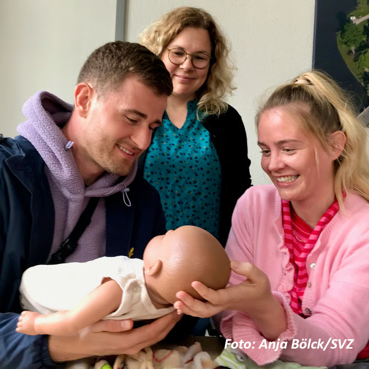 Drei Personen interagieren mit einer Babypuppe.