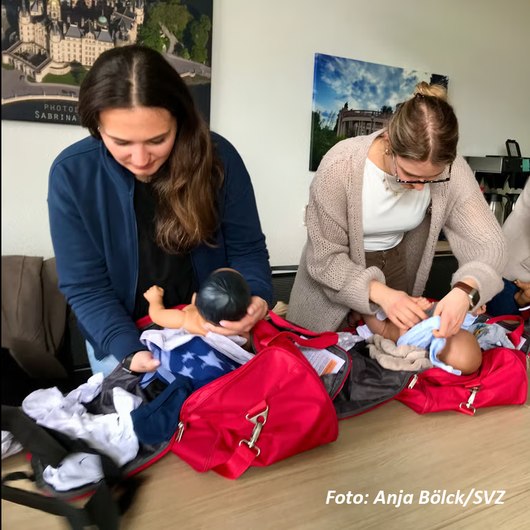 Zwei Frauen üben das Wickeln von Puppen auf einem Tisch.