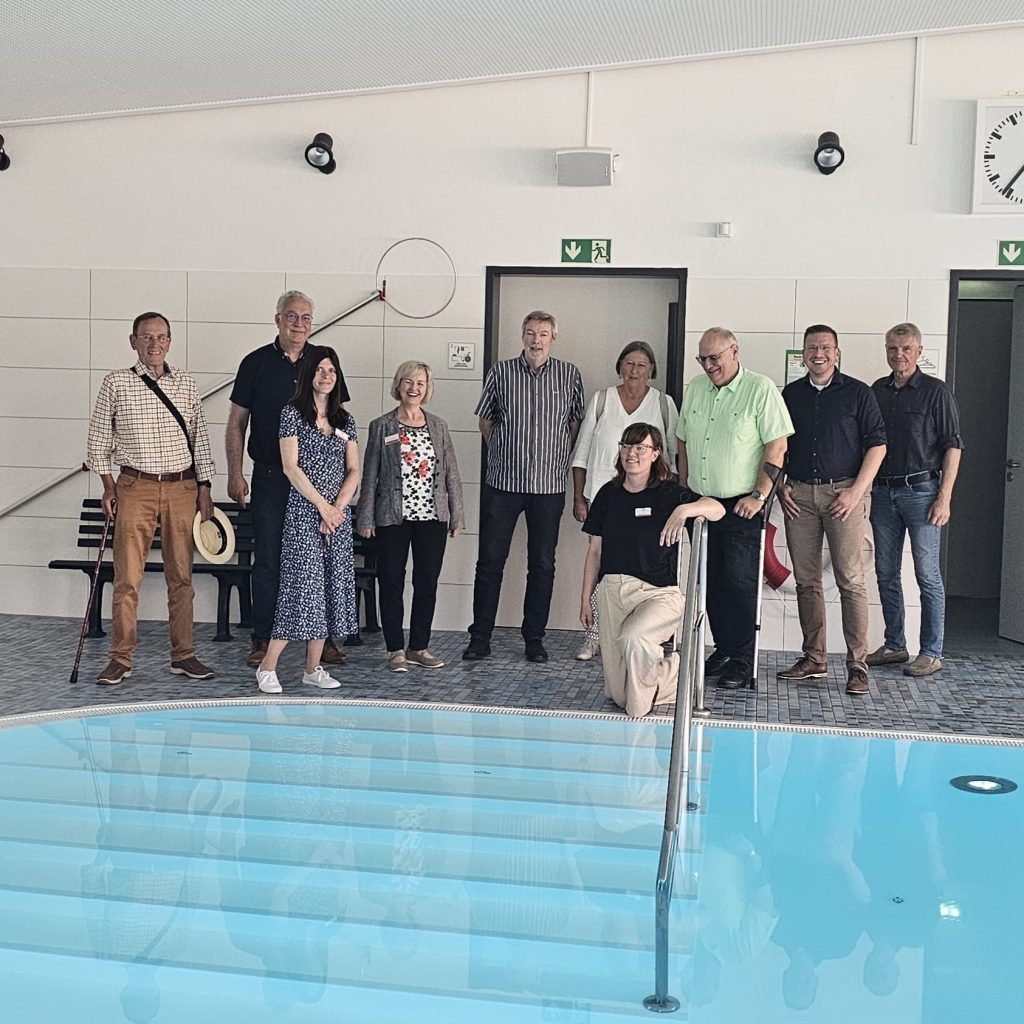 Gruppe von Menschen vor einem Schwimmbecken in einem Innenbereich