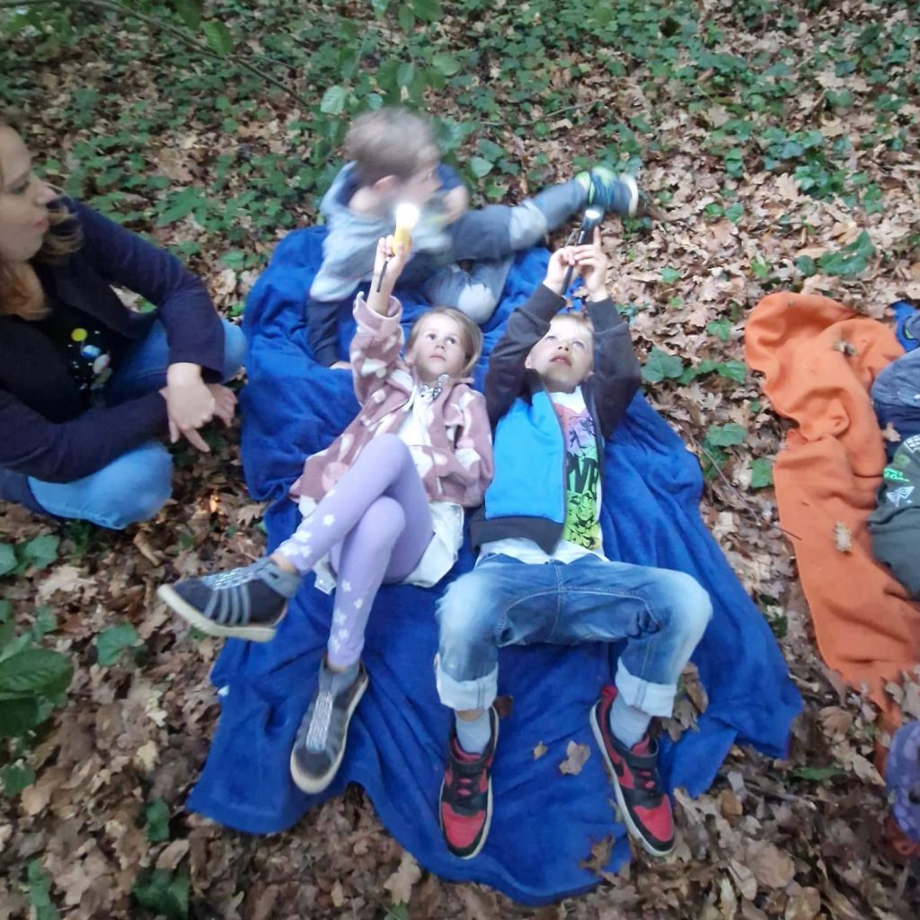 Kinder liegen auf Decken im Wald und schauen nach oben.