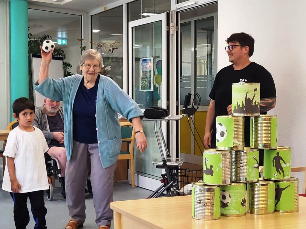 Eine ältere Frau, ein Kind und ein Erwachsener bei einem Dosenwurfspiel
