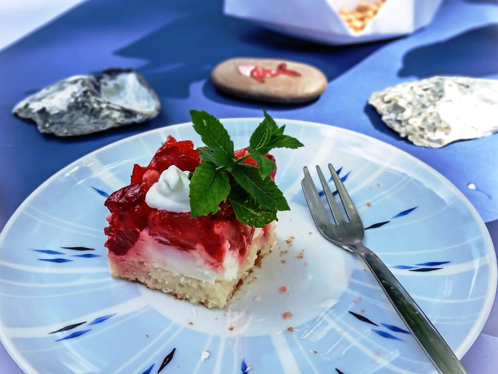 Ein Teller mit einem Stück Erdbeerkuchen, garniert mit Schlagsahne und einem Minzblatt, liegt auf einem blau-gemusterten Teller.
