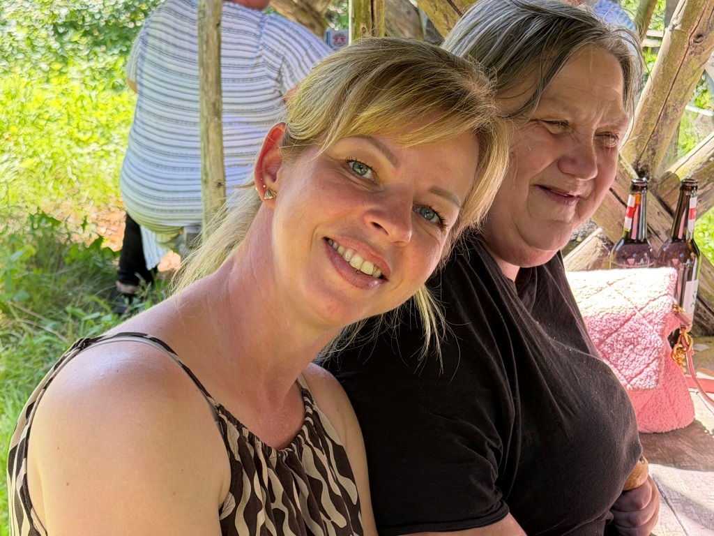 Zwei lächelnde Frauen sitzen nebeneinander in einer Gartenlaube.