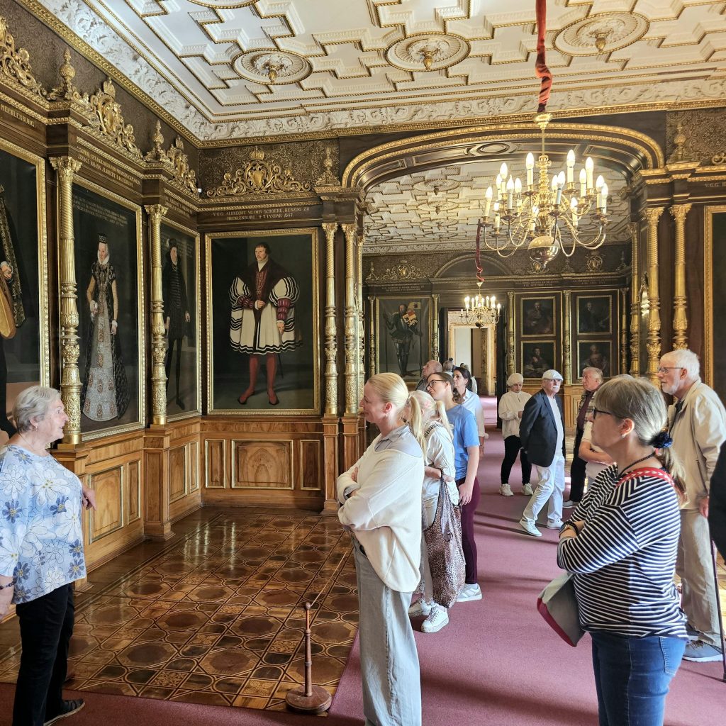 Gruppe von Menschen schaut sich Gemälde in einem historischen Raum an.