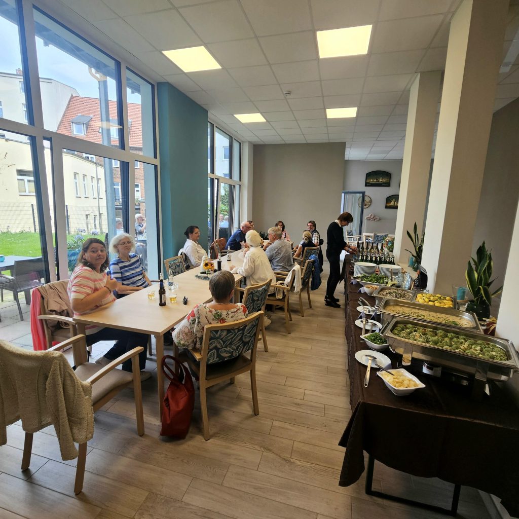 Ein Gemeinschaftsraum mit Menschen, die an einem langen Tisch sitzen und speisen.