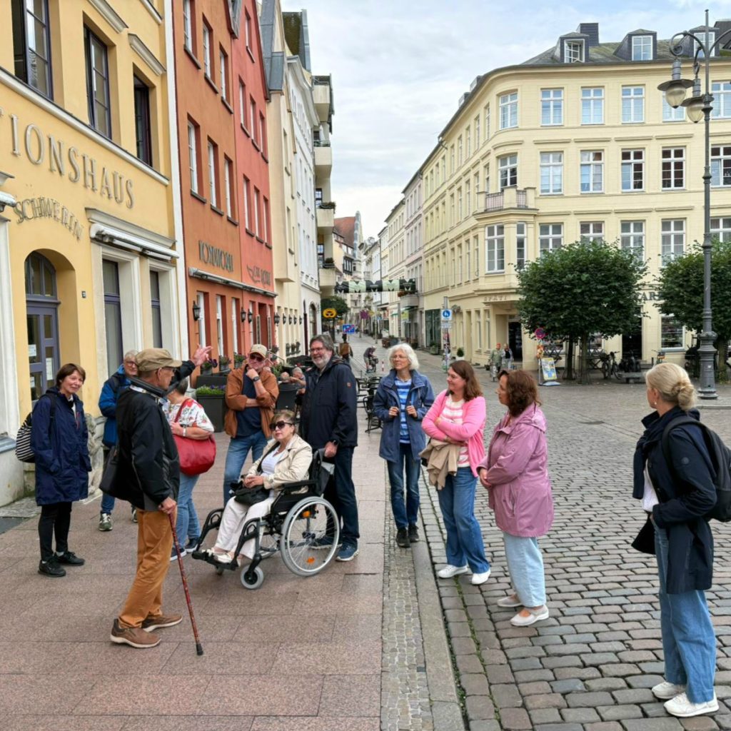 Eine Gruppe von Menschen steht auf einer gepflasterten Straße vor einer Reihe farbiger Gebäude in einer Stadt.