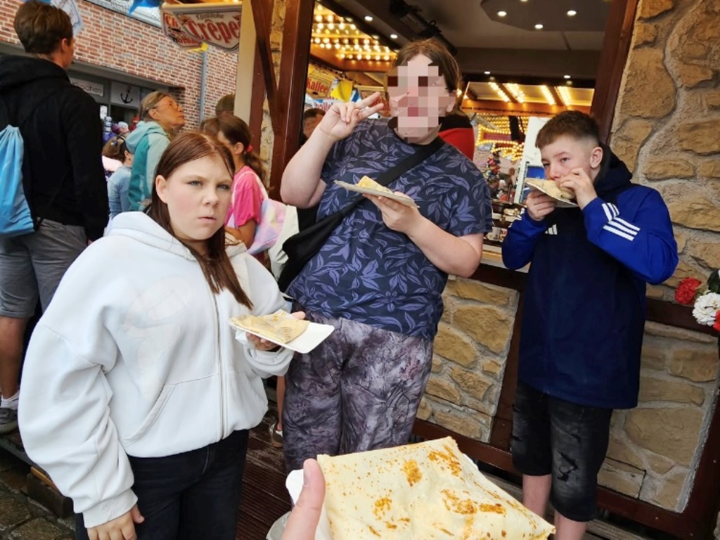 Drei Menschen essen Crêpes vor einem Crêpe-Stand auf einem Event.