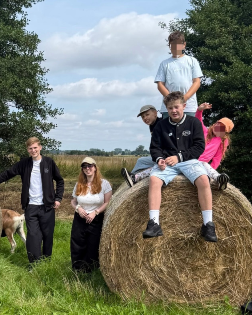 Eine Gruppe von jungen Menschen posiert auf und neben einer großen Heuballe auf einem Feld.