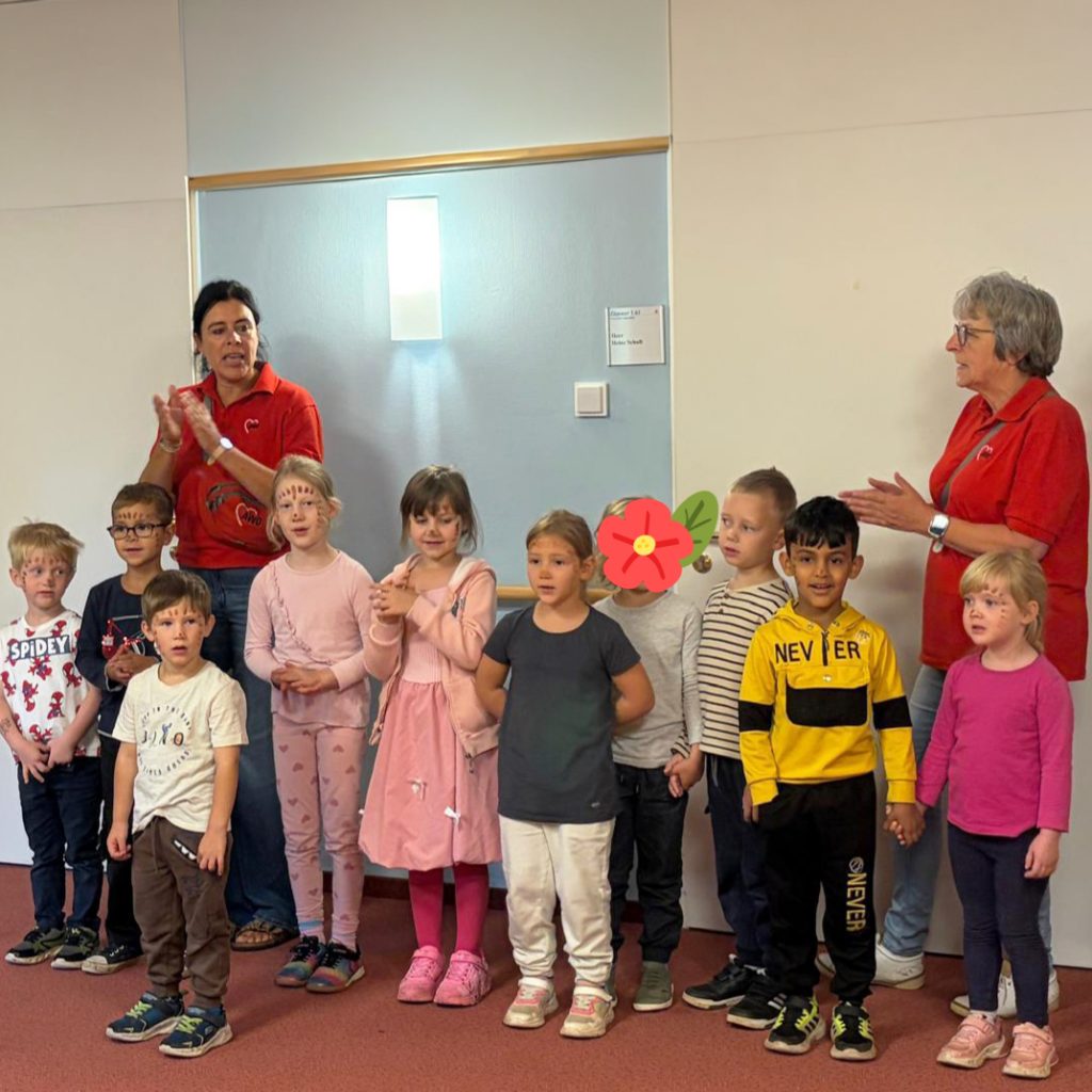 Gruppe von Kindern und zwei Erwachsenen beim gemeinsamen Singen oder Sprechen