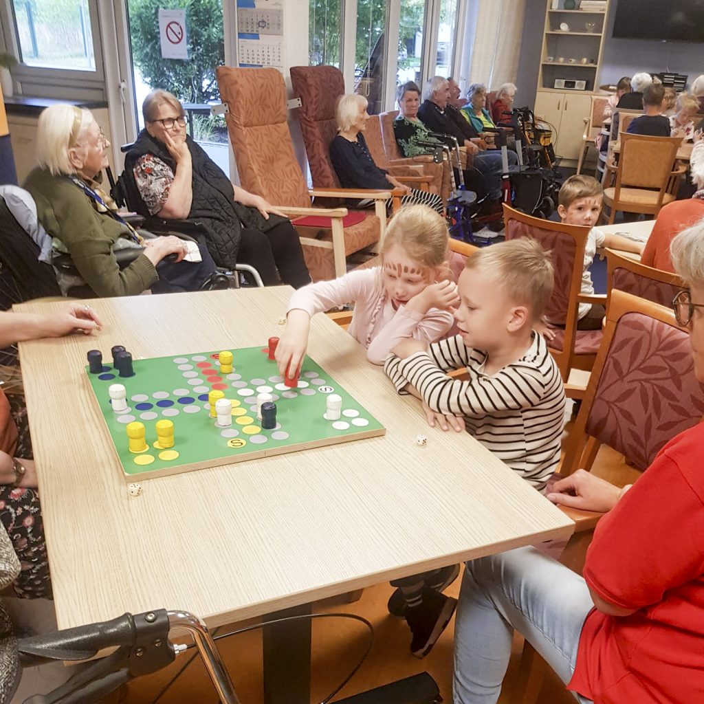 Menschen unterschiedlichen Alters spielen ein Brettspiel in einem Gemeinschaftsraum.