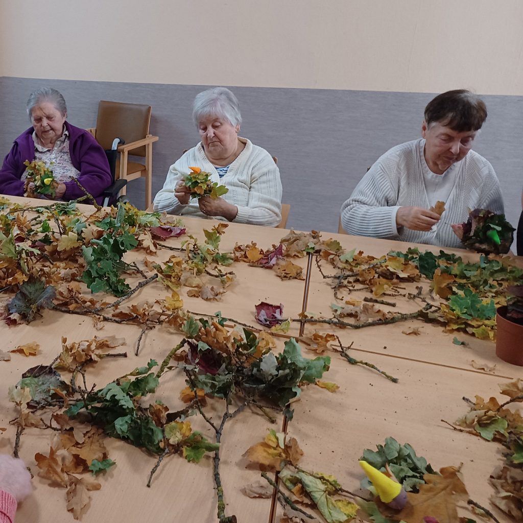 Drei ältere Frauen basteln mit Herbstlaub an einem Tisch.