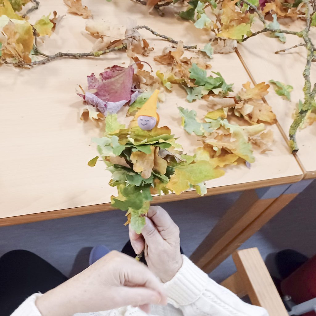 Person hält einen selbstgemachten Dekorationsgegenstand aus Herbstblättern und einem kleinen Figürchen