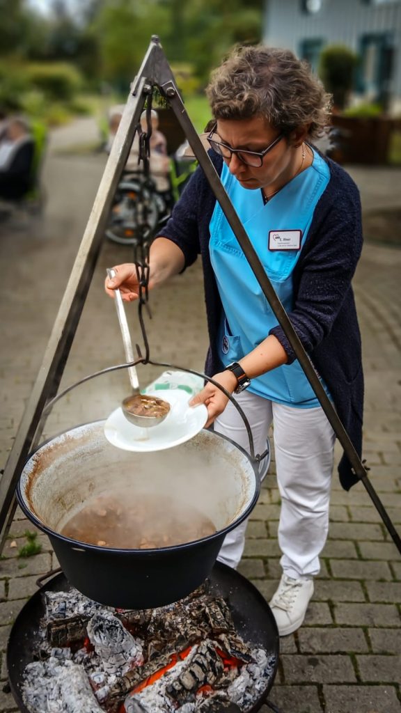 Person serving soup from a pot over an open fire.