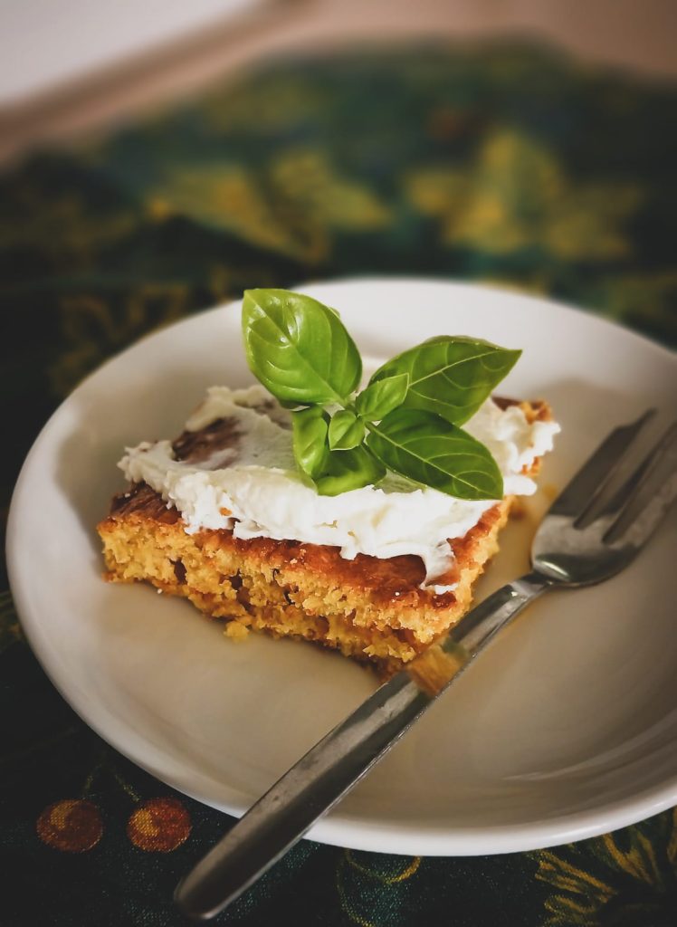 Ein Stück Kuchen mit Sahne und Basilikum auf einem Teller.