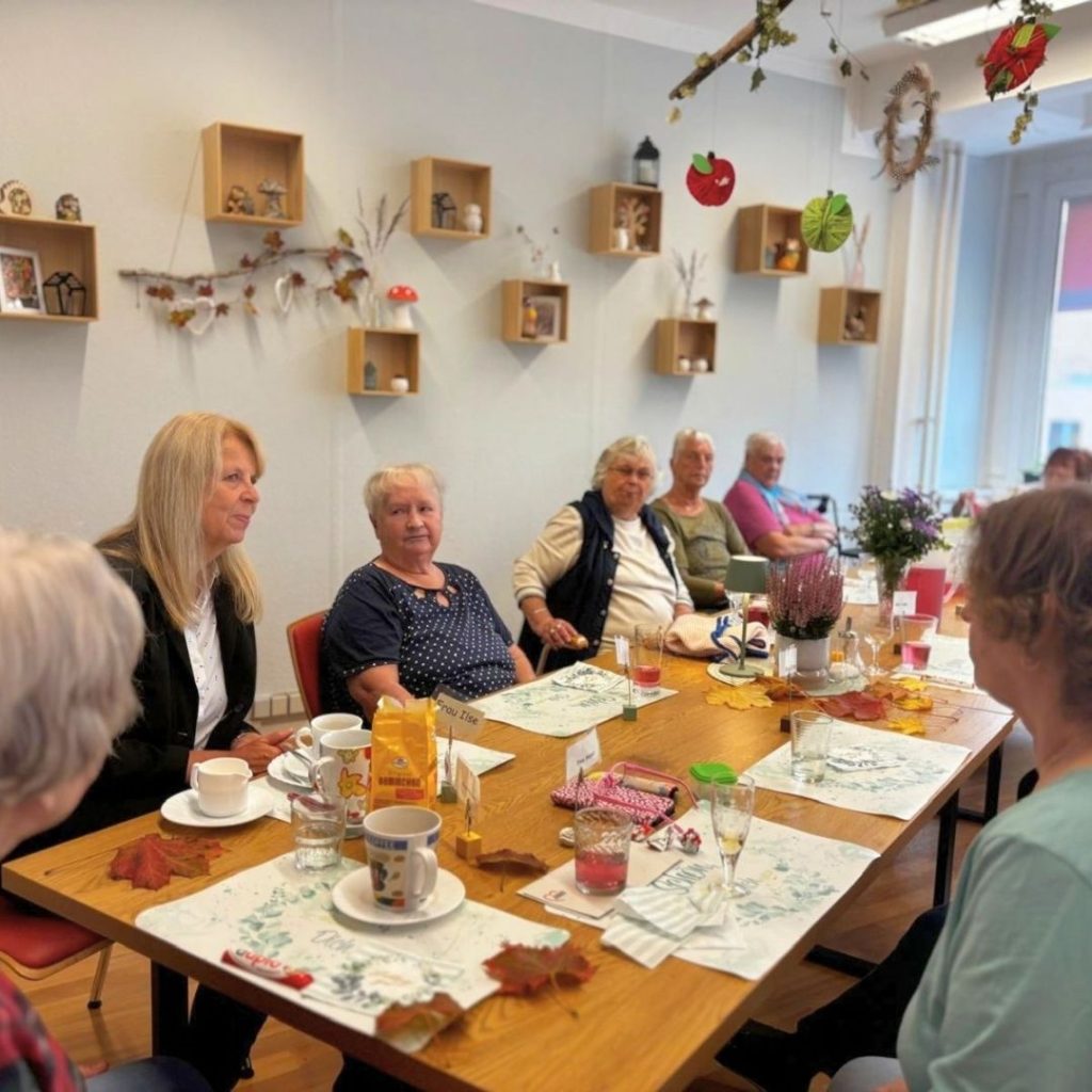 Eine Gruppe &auml;lterer Menschen sitzt an einem Tisch in einem gem&uuml;tlich dekorierten Raum.