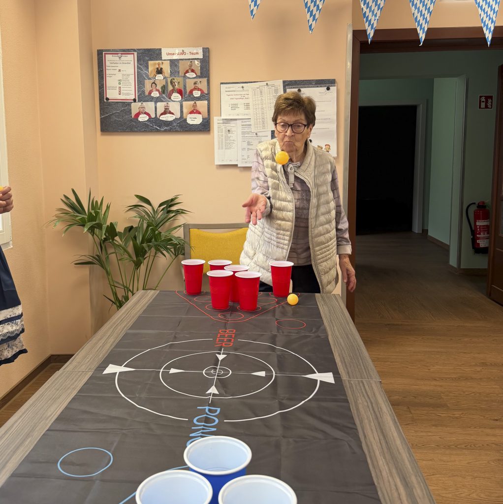 Eine ältere Dame spielt ein Geschicklichkeitsspiel mit Plastikbecher und Tischtennisball.
