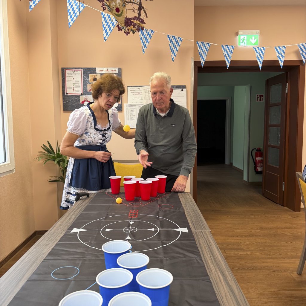 Ein älterer Mann spielt Beer Pong mit einer Frau in Tracht.