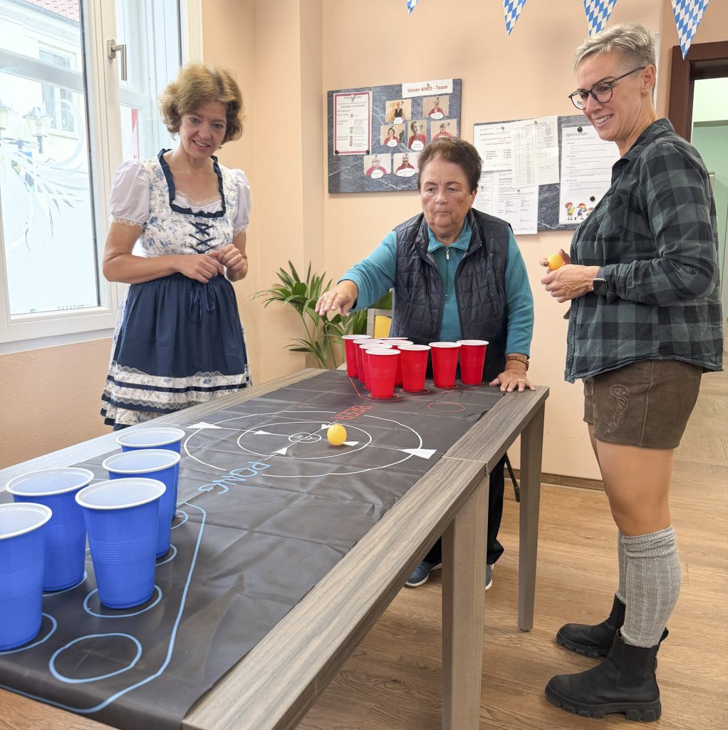 Drei Frauen spielen ein Spiel an einem Tisch mit roten und blauen Bechern und einem Tischtennisball.