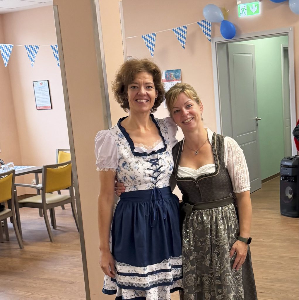 Zwei Frauen in traditionellen bayerischen Dirndln in einem Raum mit Oktoberfestdekoration.