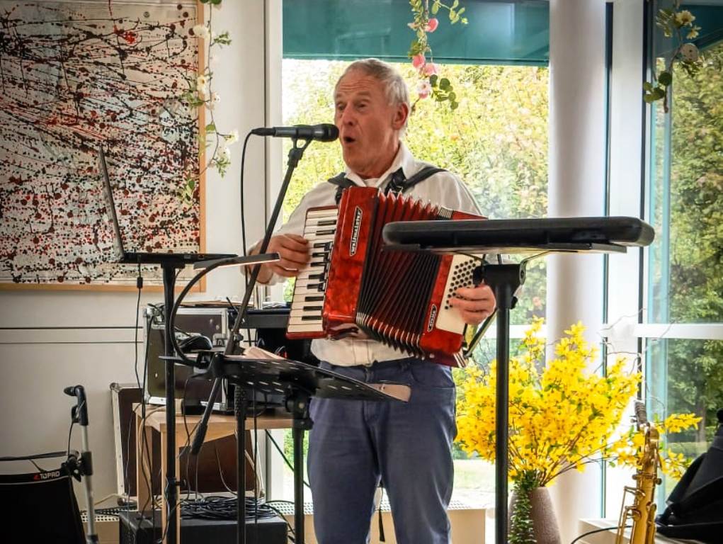 Mann spielt Akkordeon und singt in einem Raum mit Kunstwerk im Hintergrund