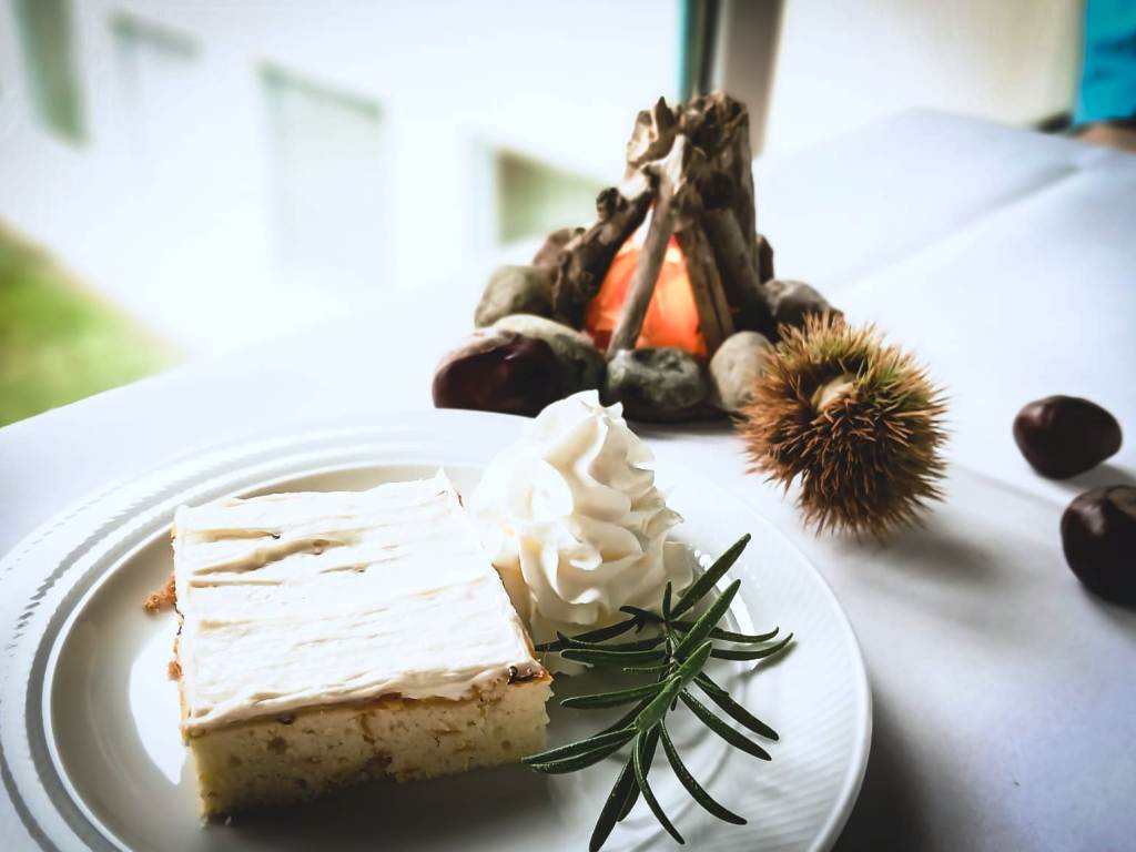Ein Stück Kuchen mit Sahne und einem Rosmarinzweig auf einem Teller, dekoriert mit Herbstmotiven.