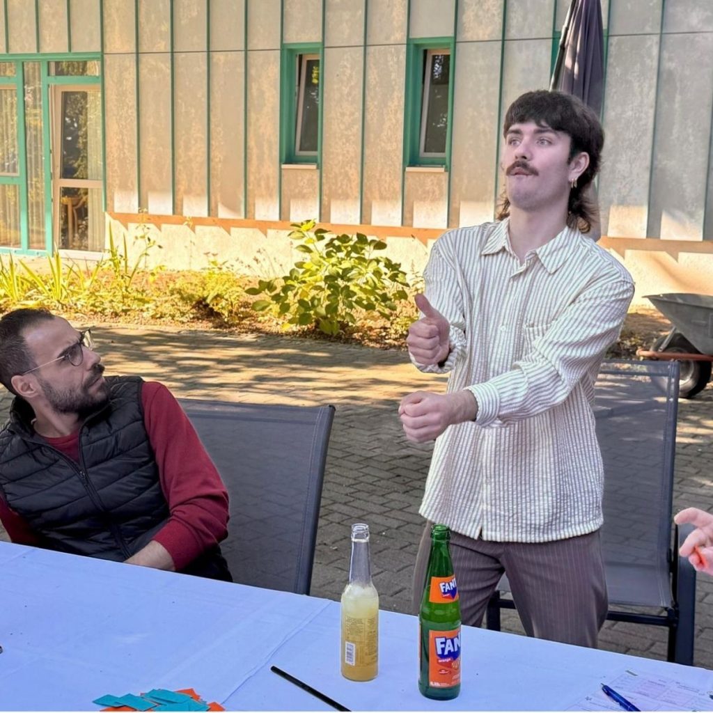 Zwei Personen im Freien an einem Tisch, von denen eine gestikuliert.